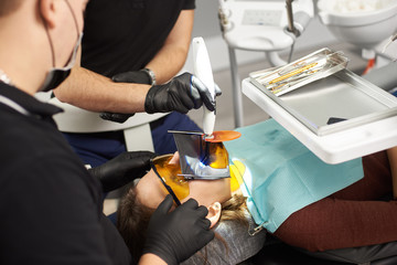 Two dentists in black suits fixing the teeth of a patient with a kofferdam on the face