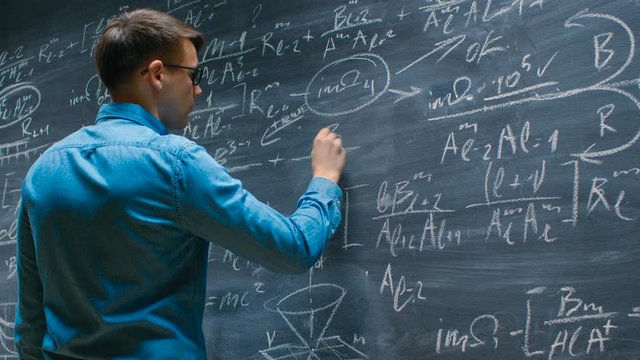 Mathematician Approaches Big Blackboard and Finishes  writing Mathematical Formula.