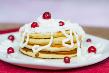 Fresh baked pancakes for Breakfast in a white plate, decorated with sour cream and cranberries, close-up