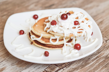 Fresh baked pancakes for Breakfast in a white plate, decorated with sour cream and cranberries, close-up