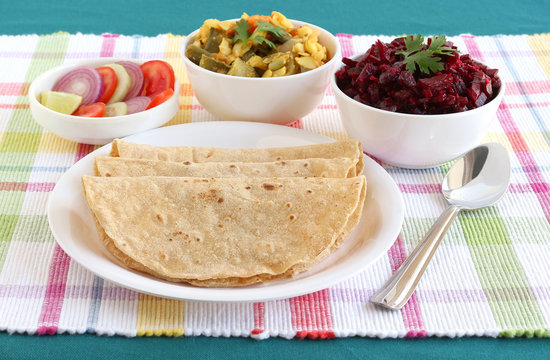 Chapati, also known as Indian flat bread, homemade without oil, India's traditional and popular vegetarian food with vegetable and beetroot curry and salad as side dishes on a table mat.