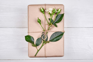 Top view of gift box with branch of fresh roses on wooden table, copy space. Holiday background, sale, shopping. Gift wrapping. Greeting card for Valentines Day, Womens Day, Mothers Day, flat lay