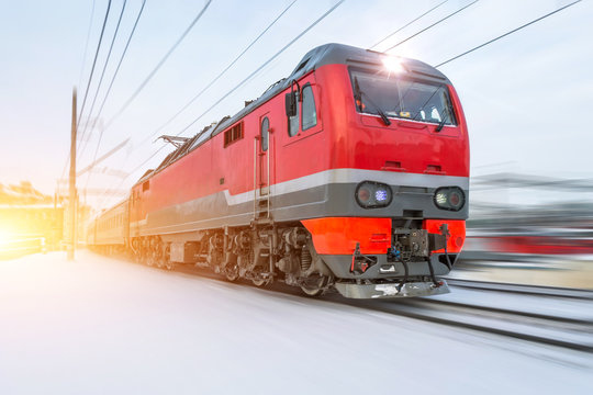 High-speed red locomotive passenger train rides at high speed in winter around the snowy landscape.