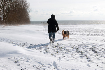 Frau mit Hund im Schnee auf dem Weg zum Meer