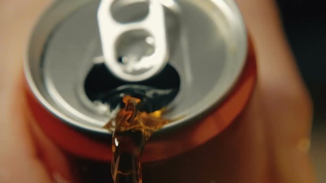 Coca-Cola is poured from a can of red color against a dark background. Slow-motion close-up shooting