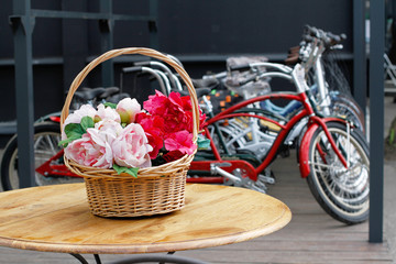 Fototapeta na wymiar Artificial peonies in a basket standing on a table on background of bicycles