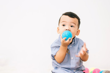 Adorable asian chubby baby boy playing a plastic ball in white living room. He feeling fun and looking to his mother and father , Happy family time on vacation concept