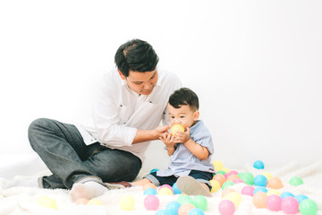 Adorable asian chubby baby boy playing a plastic ball with father in white living room , Happy family time on vacation concept