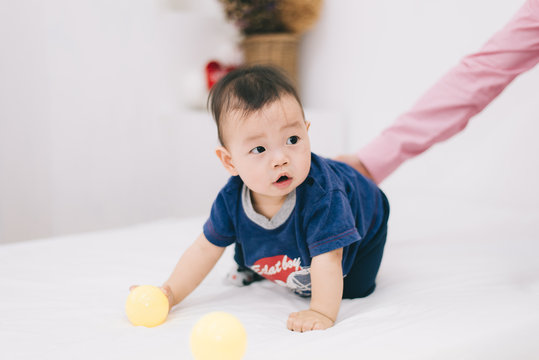 Adorable asian chubby baby boy playing a plastic ball in white living room. He feeling fun and looking to his mother and father , Happy family time on vacation concept