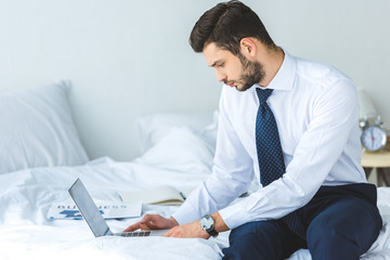 handsome bearded businessman working with laptop in bedroom