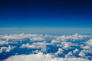 Fototapeta na wymiar Blue sky and clouds below from airplane window