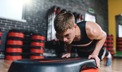 Horizontal shot of athlete man doing on stepper pushups in aerobic fitness club. The handsome male...