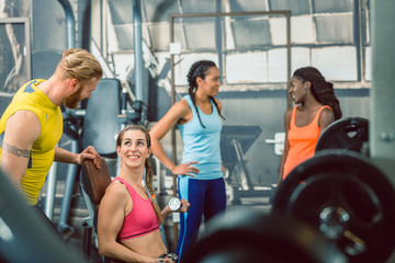 Side view of a handsome personal trainer guiding his female client while exercising with a small dumbbell for toned arms at the gym