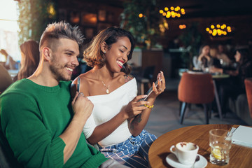 Two happy mixed race couple having fun at the coffee shop using digital tablet and credit card for online shopping.