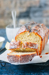 Homemade lemon poppy seed pound cake with glaze on a wire rack. Blue stone background.