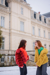 Laughing girls in red and yellow fur coats stand before an old house outside