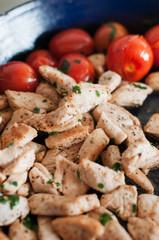 Lean strips of chicken breast browned with olive oil and seasoned with pepper and fresh parsley and basil with glazed cherry tomatoes in pan for healthy, low carb and low calorie dish