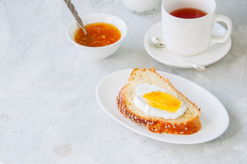 Slice of homemade sesame seeds challah bread  with jam, glass of milk and a cup of tea on a white background.