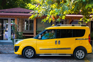 Obraz premium yellow car (station wagon) taxi in the parking lot under the green maple