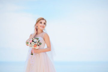 Fototapeta na wymiar Charming bride in peach dress smiles posing before a great sea view in a sunny day