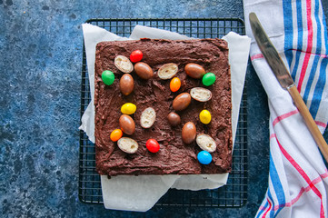 Dark chocolate brownie square on a wire rack decorated with creamy chocolate eggs. Blue stone...