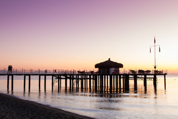 Obraz premium The bungalow on the pier is flooded with sunlight. Lilac from the dawn sky.