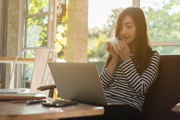Naklejka premium Beautiful young teenage woman freelance work with laptop have coffee at coffee shop in with sun light, freelance lifestyle conceptual