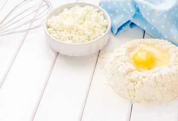Baking cake in rustic kitchen - dough recipe ingredients eggs, flour, milk, butter, sugar on white planked wooden table from above. Background layout with free text space