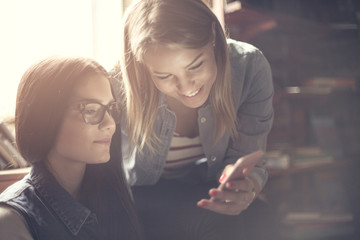 Two friends sitting at home and reading funny messages on mobile phone.