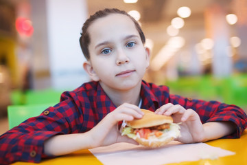 Cute smiling little girl eats a hamburger