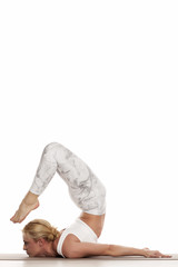 Yoga, sport, training and lifestyle concept - Young blonde woman doing yoga exercise. Portrait of young beautiful woman in white sportswear doing yoga practice.Chin stand/ Ganda bherudasana