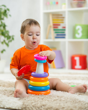 Funny baby toddler plays with pyramid toy sitting on soft carpet in nursery