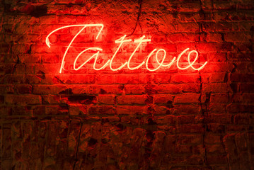 Glowing red neon signboard word tattoo on a brick dark background.