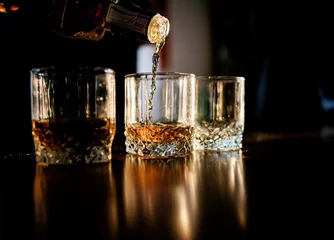 Fotobehang Man pours whisky in the glasses standing before a wooden table © IVASHstudio