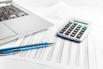 pen, calculator and laptop lying on a financial report with number charts on the desk in the office, concept for business, finance and taxes, copy space