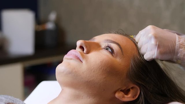 Woman in cosmetology cabinet. Cosmetologist is doing injection. woman receives an injection in the head. The concept of mesotherapy.