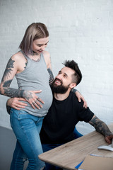smiling tattooed boyfriend hugging pregnant girlfriend at home