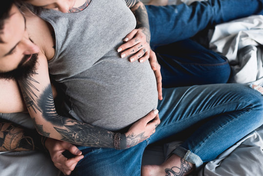 cropped image of boyfriend hugging pregnant tattooed girlfriend at home