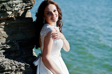 Fototapeta na wymiar Charming bride near rock with sea landscape.