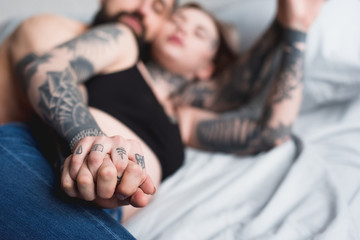 tattooed couple holding hands on bed