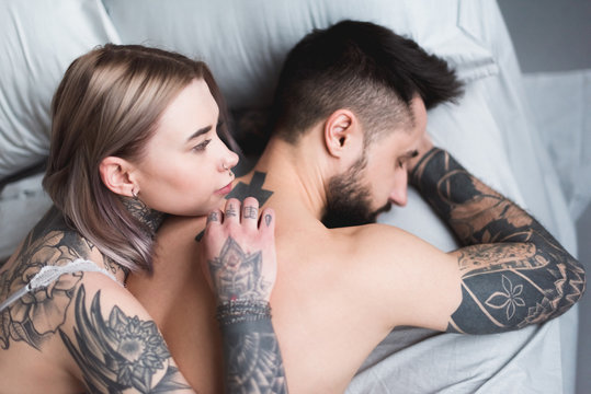 high angle view of tattooed shirtless couple lying on bed