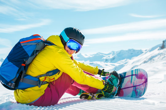 Image of woman in helmet with backpack sitting in snow with snowboard