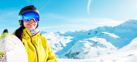 Panoramic image of woman in helmet and with snowboard against background of snowy landscape