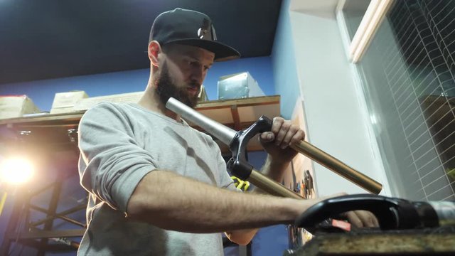 A man bike mechanic with a beard assembles a mountain bike in his workshop.