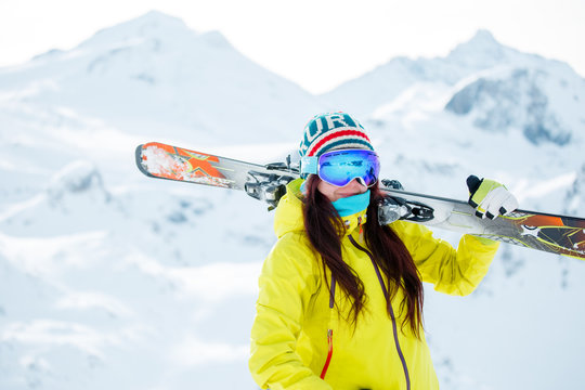 Picture of sporty woman with skis on her shoulder against background of snowy hill