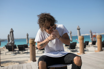 Stylish man sitting near the beach and smoking.