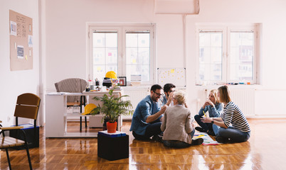 Young happy innovative business people sitting on the floor of the office in the circle and brainstorming with pleasure. Teamwork and togetherness concept.