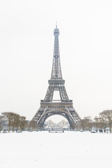 Winter in Paris in the snow. The Eiffel tower seen from the Champ de Mars, with a snow covered lawn in the foreground and the top of the tower disappearing slightly in the mist.