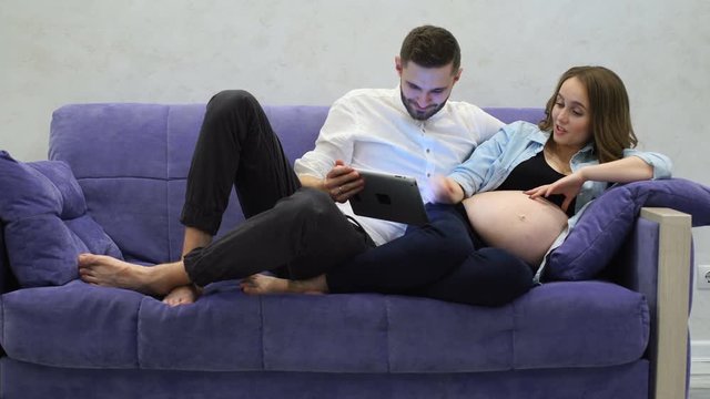 A happy married couple chooses clothes in an online store for their booming baby. A pregnant woman with her husband uses a touch-sensitive tablet computer. Online shopping for a young child. Choosing