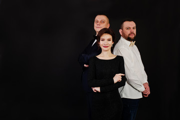 Elegance woman in black evening dress with two man in suit posed on studio isolated on black. Trio band.